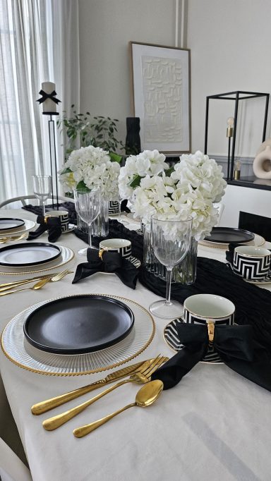 Décoration de table élégante noir et doré – Table enchantée Table élégamment dressée avec fleurs blanches, assiettes noires et dorures raffinées.