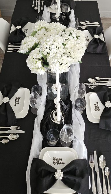 Décoration de table noir et blanc chic – Idée anniversaire élégant Table élégamment dressée avec vaisselle blanche, nappes noires et centre de fleurs blanches.