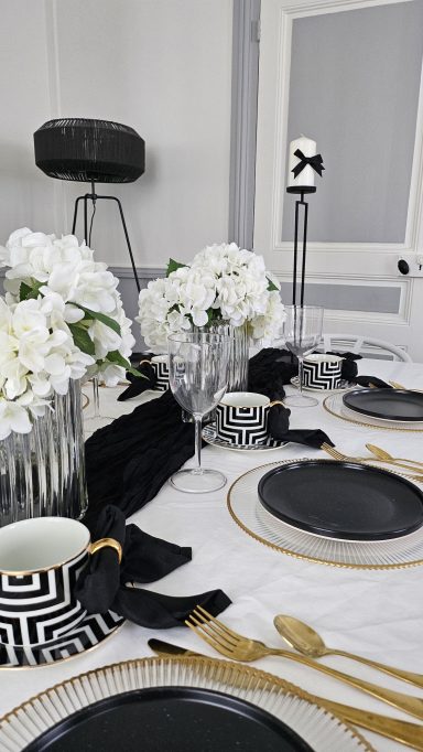 Décoration de table élégante noir et doré – Table enchantée Table élégamment dressée avec fleurs blanches, assiettes noires et couverts dorés.