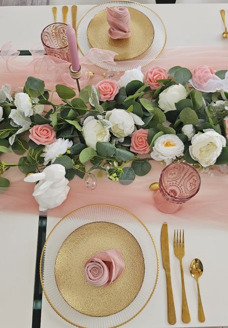 Décoration de table rose et doré Table élégamment dressée avec nappe rose, fleurs, assiettes dorées et couverts raffinés.