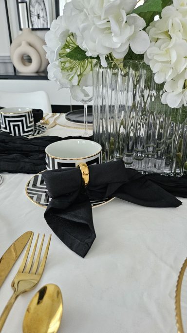 Décoration de table élégante noir et doré – Table enchantée Une table élégamment dressée avec des fleurs blanches et des serviettes noires.