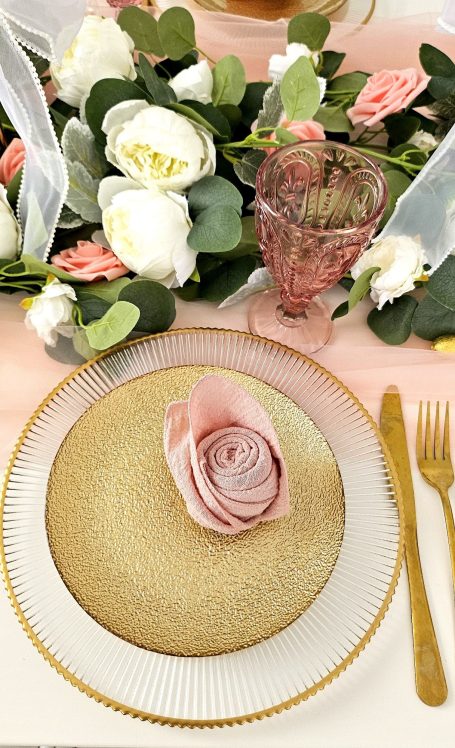 Décoration de table rose et doré Assiette élégante avec une rose en tissu et des fleurs fraîches en arrière-plan.