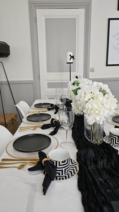Décoration de table élégante noir et doré – Table enchantée Table élégante dressée avec des assiettes noires, des fleurs blanches et des accessoires noirs.
