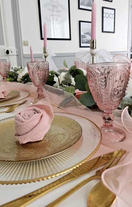 Décoration de table rose et doré Table élégamment dressée avec des roses en tissu, couverts dorés et verres roses.