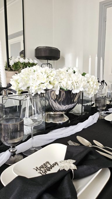 Anniversaire noir et blanc Table dressée avec fleurs blanches, verres, couverts et nappe noire élégante.